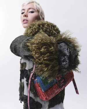 Iris Law wearing a textured olive fur jacket and a sequined Fendi Baguette shoulder bag against a white studio background.