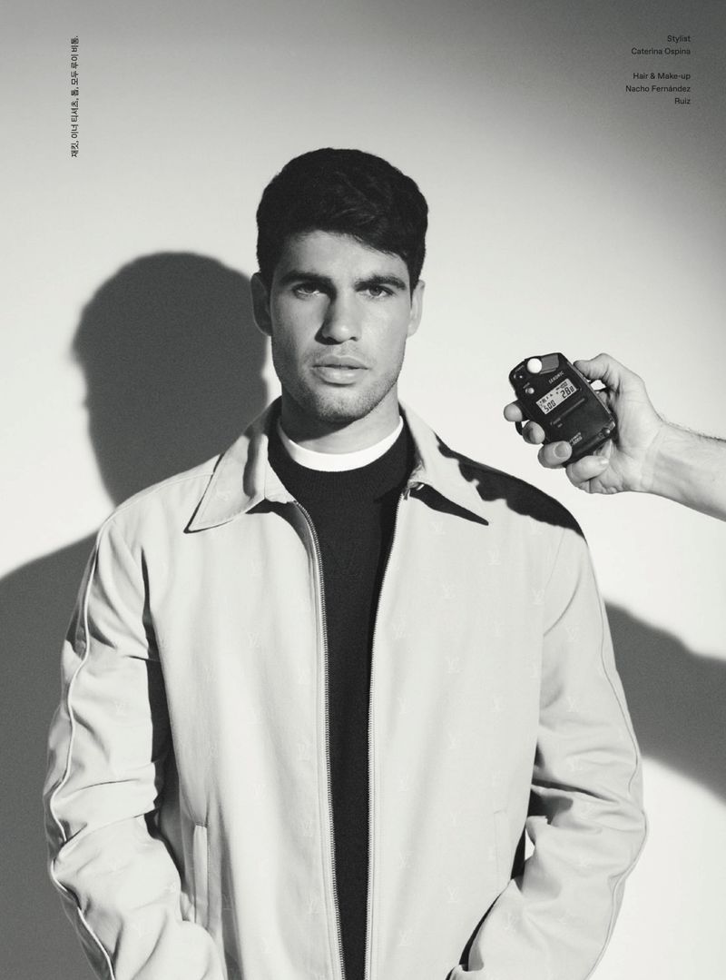 A monochrome portrait of a young adult man in a jacket, with a light meter being held next to his face in a photo studio.