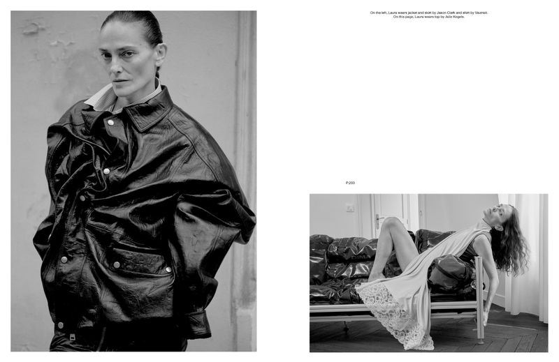 Black-and-white fashion shot featuring a woman in a large leather jacket and another woman reclining on a sofa in the background.