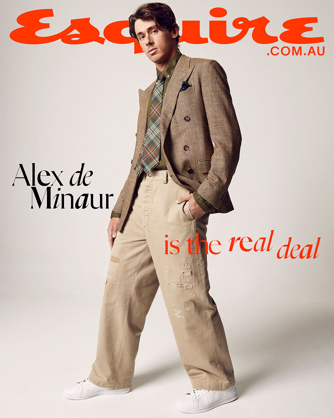 Magazine cover featuring a stylish adult male in a double-breasted blazer, beige trousers, and white sneakers against a neutral backdrop.