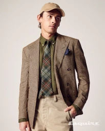 Alex De Minaur wearing a houndstooth blazer, green shirt, plaid tie, and a beige cap against a neutral studio backdrop