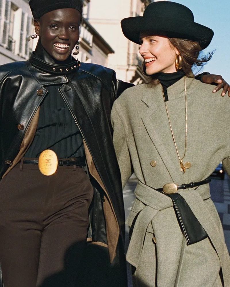 Two smiling models walking outdoors wearing stylish coats and hats in a British Vogue fashion editorial titled Riding High.