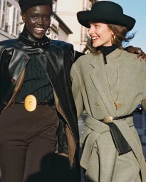 Two smiling models walking outdoors wearing stylish coats and hats in a British Vogue fashion editorial titled Riding High.