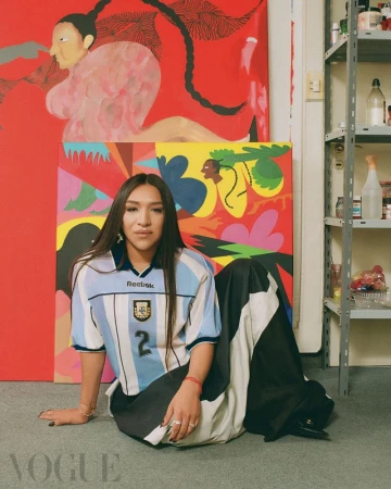 Person in a vintage Argentina national football team jersey and wide skirt seated in front of vibrant artwork.