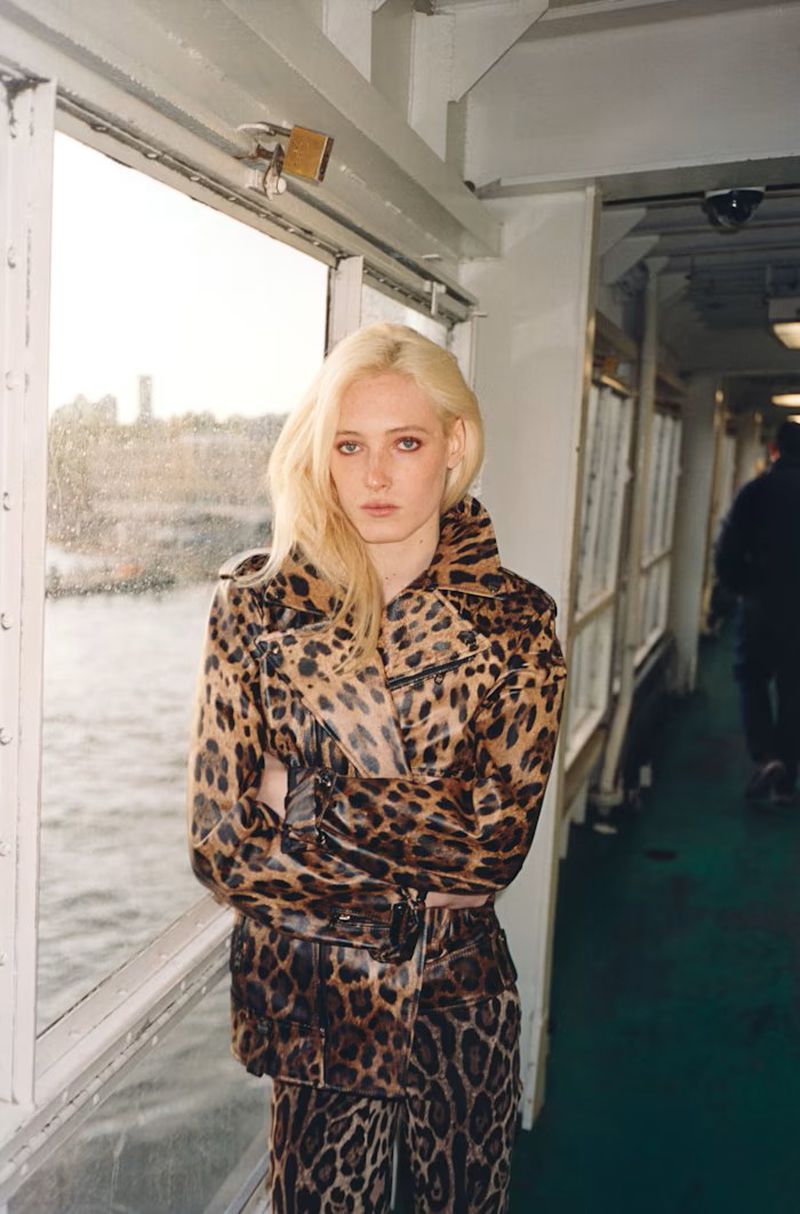 Summer Dirx wearing a leopard print leather jacket while standing next to a ferry window overlooking the water.