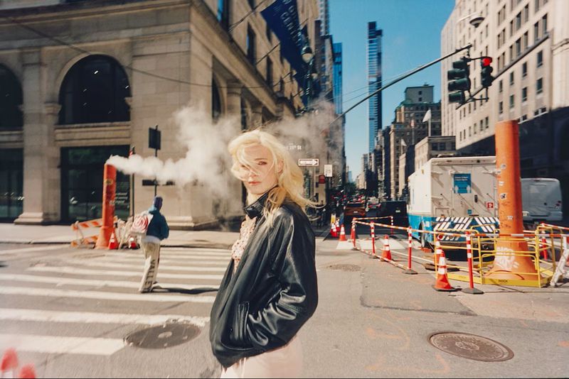 Model Summer Dirx wearing an oversized black leather jacket on a sunlit New York City street with steam rising in the background.