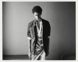 Black and white portrait of a young man wearing a dark jacket, unbuttoned white shirt, and patterned silk scarf tied at the waist.