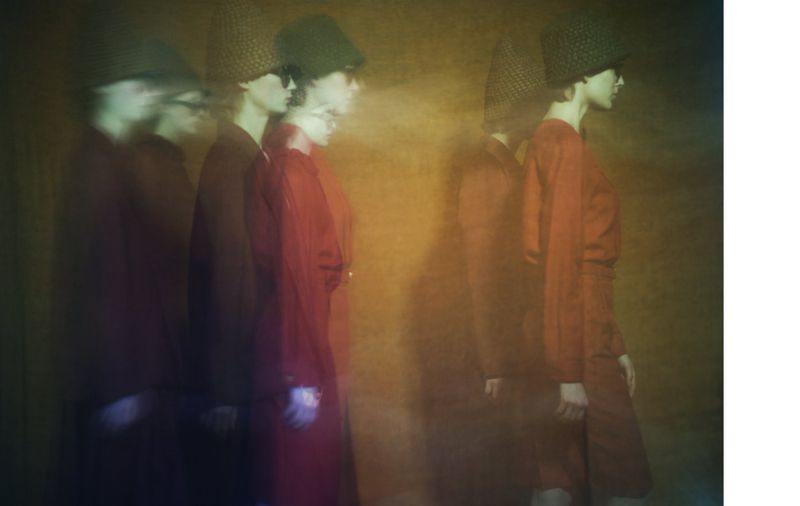 Fashion shot of a blurry group of women wearing similar outfits and hats in a studio with an orange and brown mottled background.