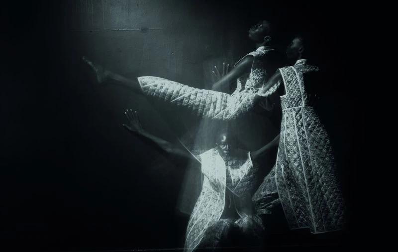 Monochrome portrait of a Black woman in motion, wearing an ornate dress. She is captured in multiple transparent overlapping images.