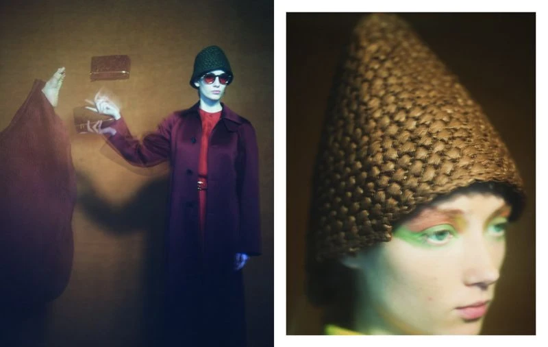 A woman in a maroon coat and green hat holds a purse in a studio with warm lighting and a blurred figure, creating a vintage, fashion-forward aesthetic.