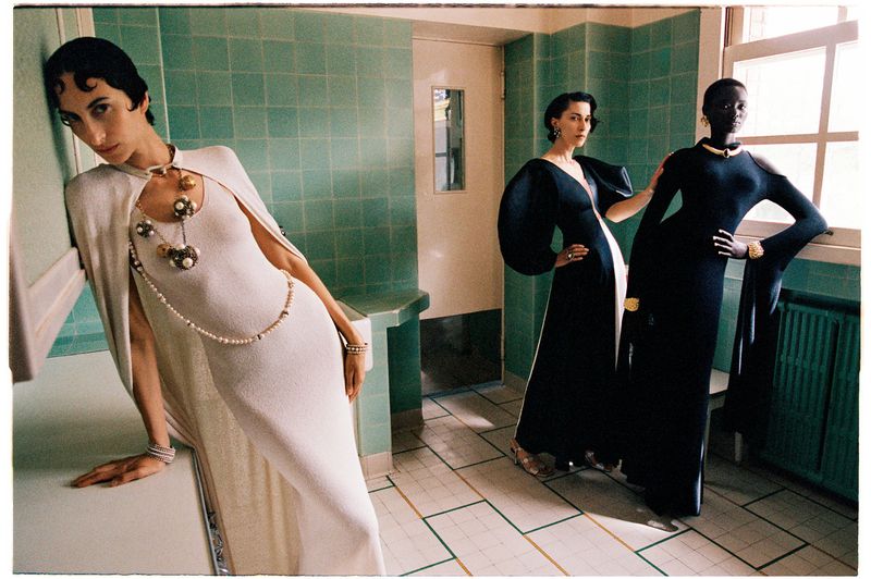 Model in a white cape gown leaning in a green-tiled room beside two models in black evening dresses for Vogue Scandinavia.