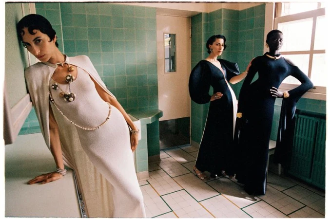 Model in a white cape gown leaning in a green-tiled room beside two models in black evening dresses for Vogue Scandinavia.