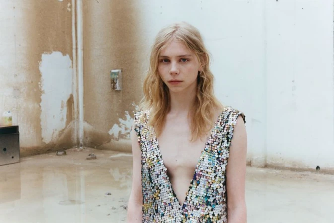Model Rafe Crane-Robinson wearing an iridescent plunging sequin top against a distressed concrete wall with standing water.