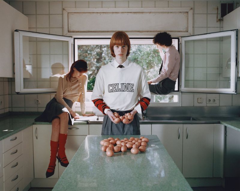 Fashion editorial shot in kitchen setting features androgynous model holding eggs with 2 other models in the background.