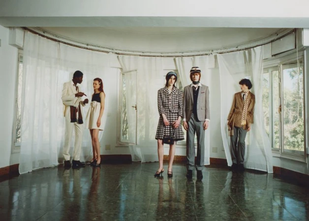 A group of fashion models in vintage clothing poses in an airy room with natural light, showcasing a retro aesthetic and classic style.