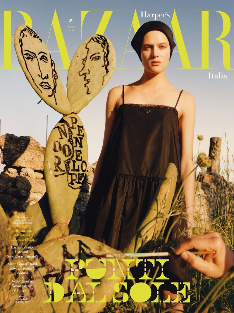 Model in a black dress and dark head covering standing beside a painted prickly pear cactus in sunlight