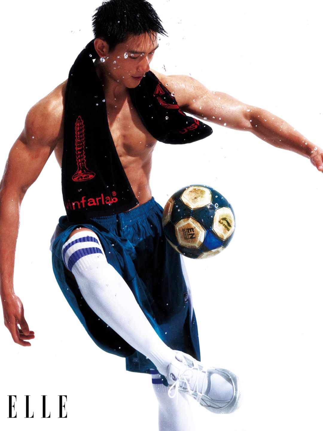 Shirtless male athlete juggling a soccer ball with a towel around his neck against a plain white background for Elle China World Cup editorial.