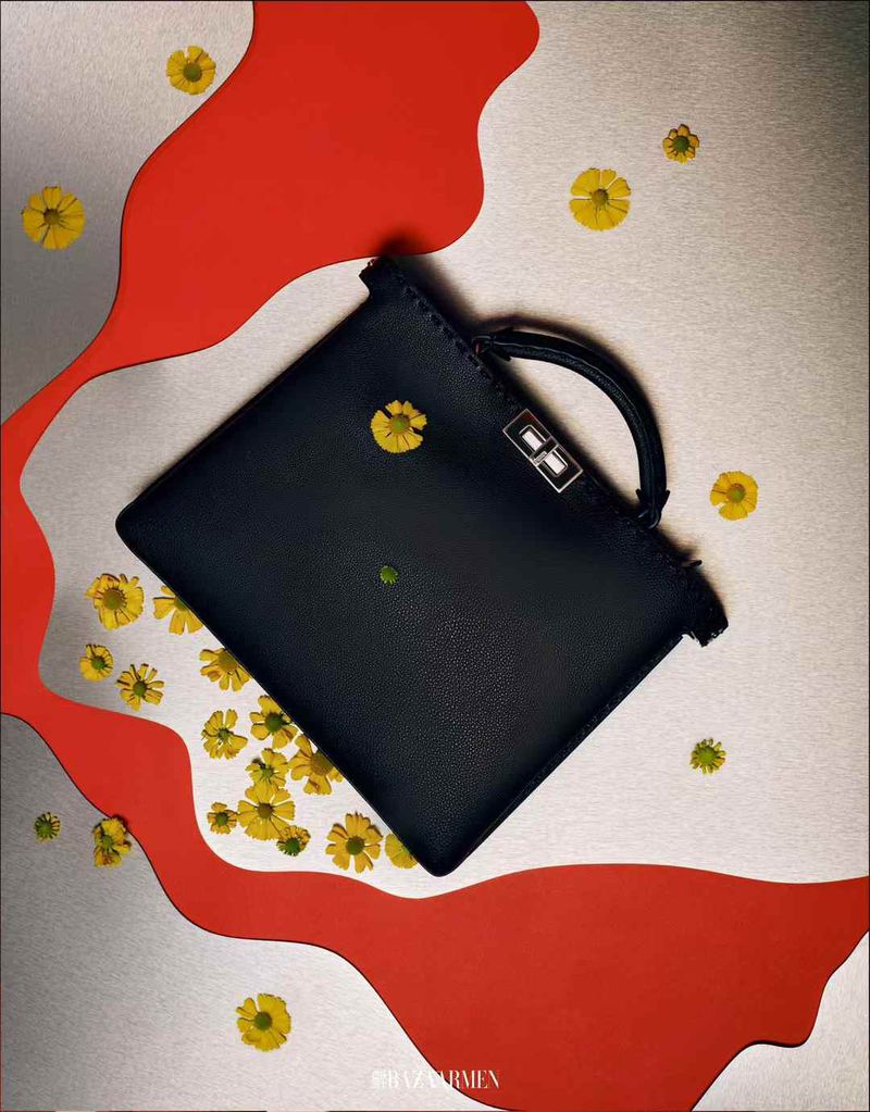 Close-up shot of a navy-blue leather handbag decorated with small yellow flowers, placed on a silver backdrop with red wavy lines.