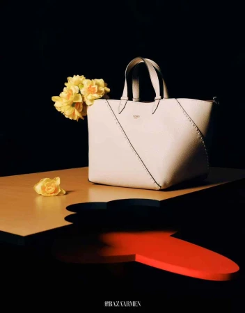 Elegant tote bag on a table with yellow flowers against a black background, illuminated by soft light in a studio setting.