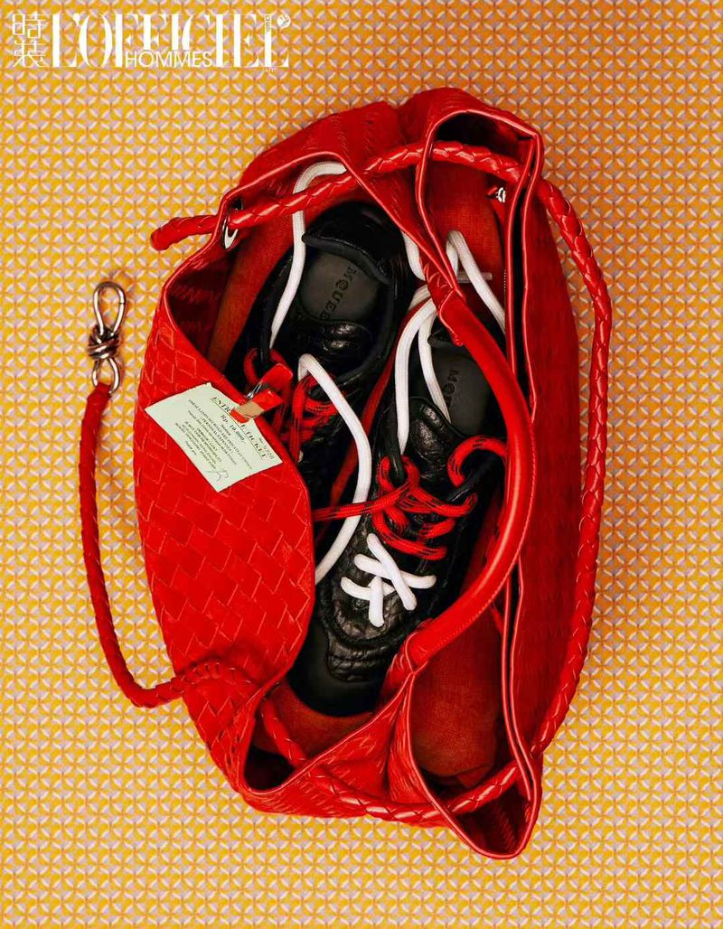 Red woven drawstring bag with a pair of black sneakers with red and white laces on a yellow patterned background.