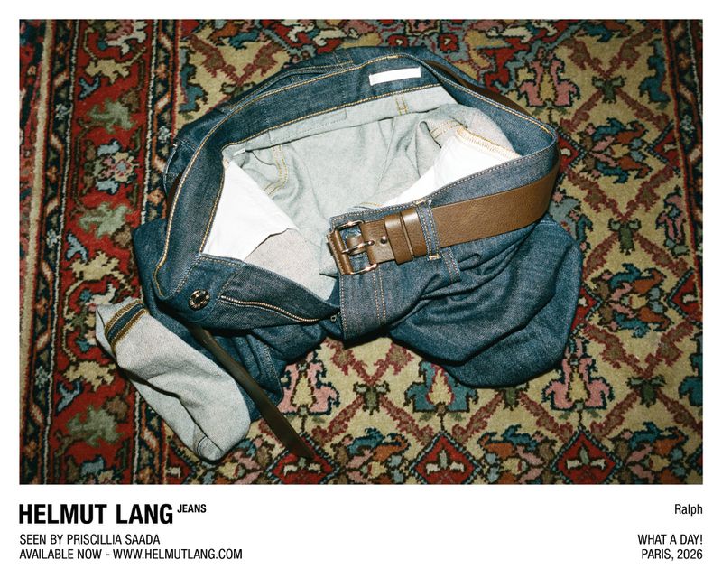 Helmut Lang denim jeans with a brown leather belt laid crumpled across an ornate patterned oriental rug.