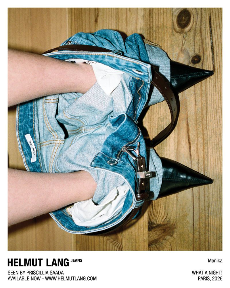 Close-up of blue denim jeans bunched around ankles with black pointed high-heel shoes on a wooden plank background.