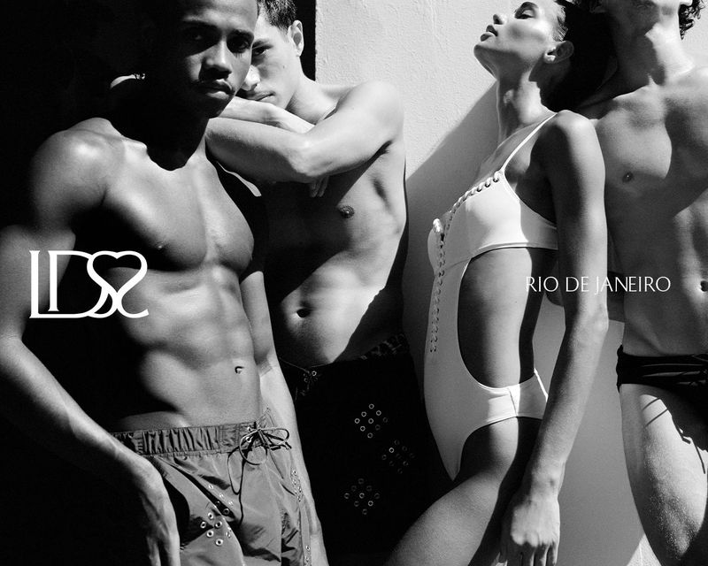 Four models posing in swimwear under harsh sunlight and sharp shadows in a high-contrast black and white shot.