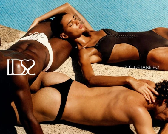Three models in black and white swimwear sunbathing poolside in bright direct sunlight.