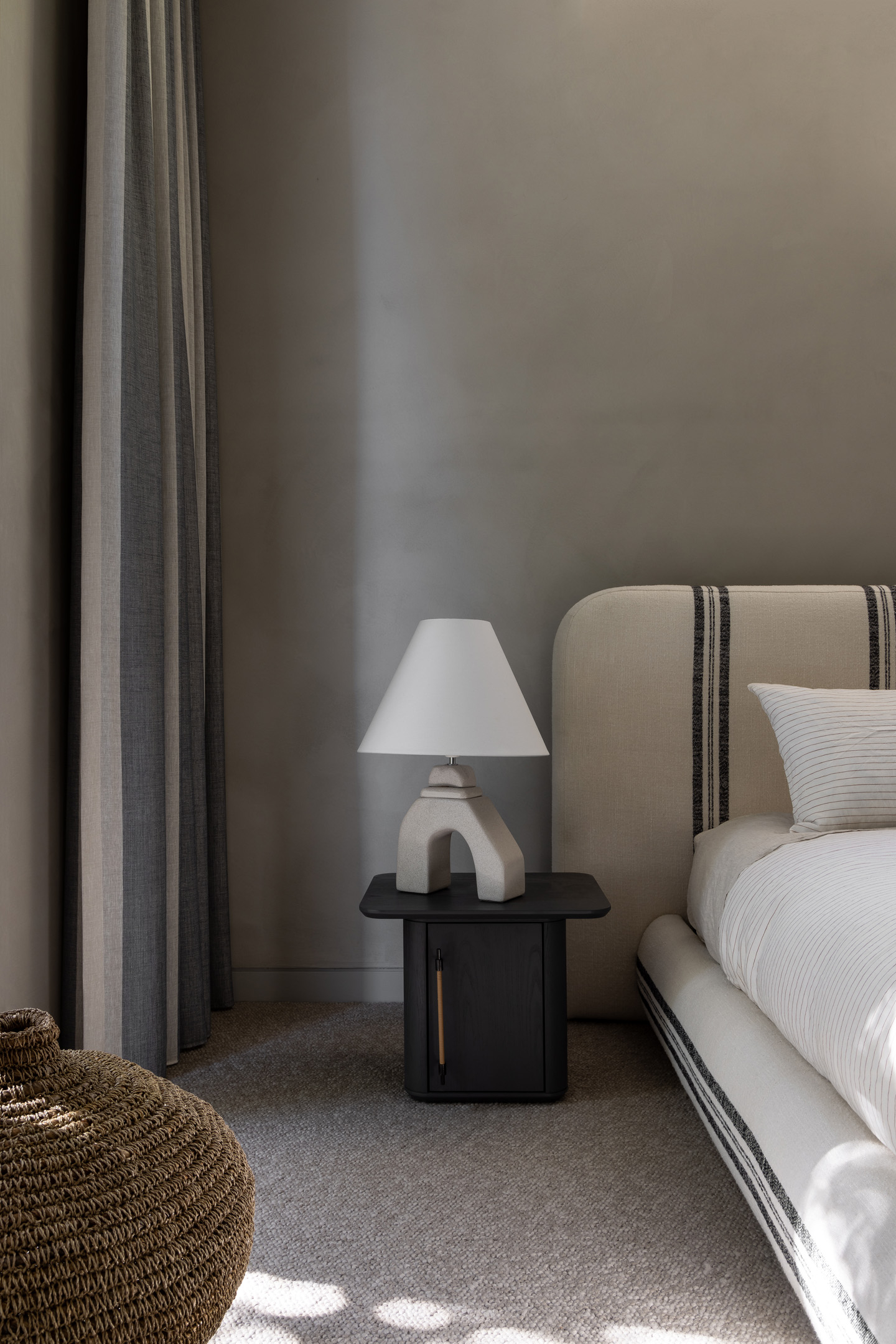 Interior view features a modern bedroom with a striped headboard, minimalist bedside table, and neutral color palette.
