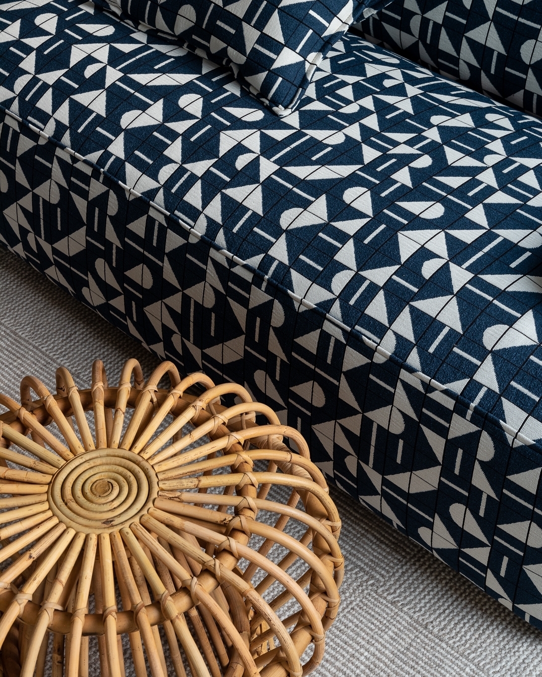 Close-up of a patterned couch in navy and white paired with a round woven rattan side table on a grey patterned carpet.