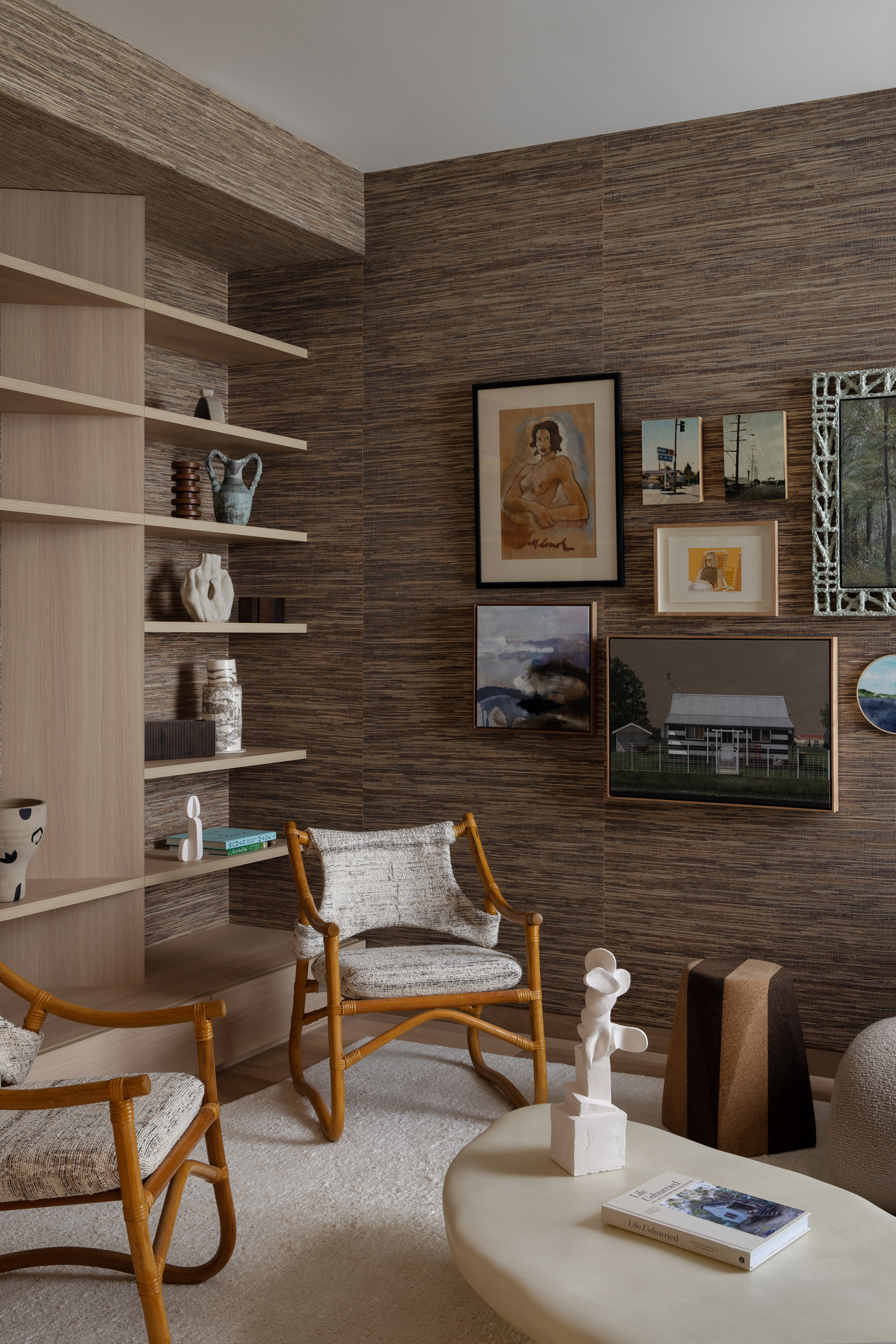 Living room interior featuring two wooden chairs, a light-colored rug, and a decorative arrangement of artwork and objects on shelves.