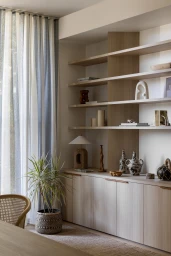 Built-in wooden shelving and cabinetry with decorative vases, lamp, and a potted plant in a modern interior setting