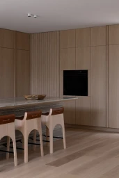 Minimalist modern kitchen interior with light wood cabinetry, a stone island, and matching wooden barstools.