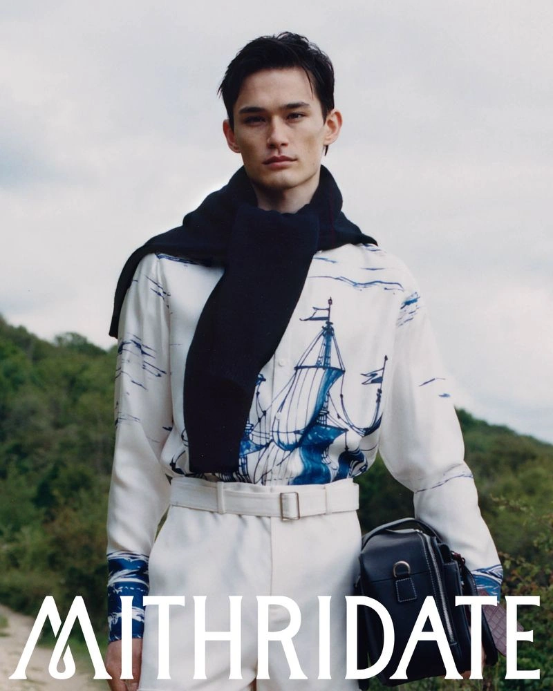 Model wearing a printed shirt and dark sweater outdoors with hills in the background for Mithridate Pre Fall 26 campaign