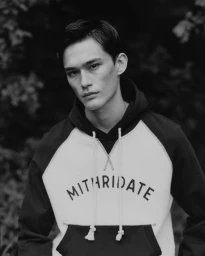 Model Alex Schlab in a black and white Mithridate raglan hoodie posing against a soft-focus outdoor background.