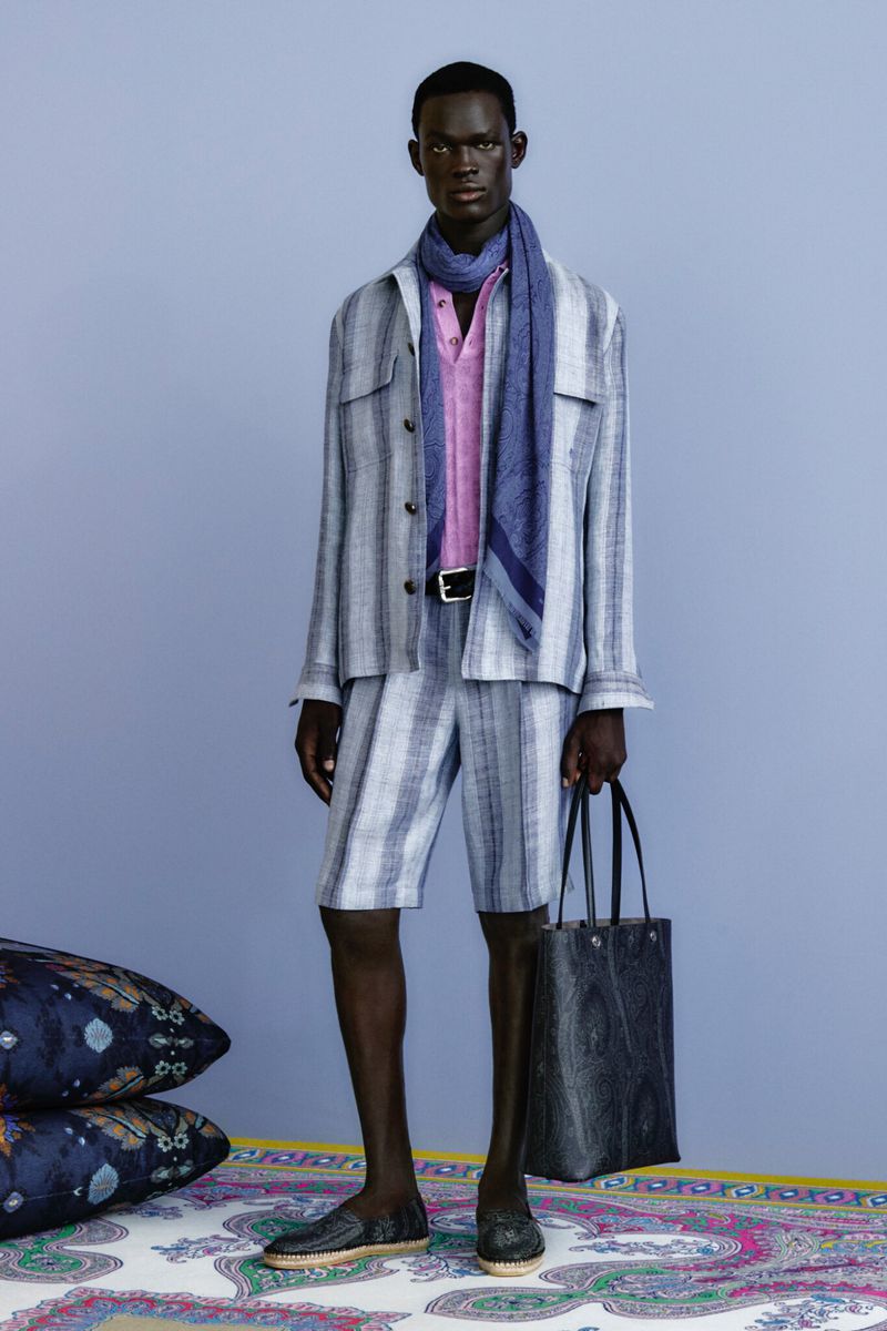 An African-American male model poses indoors wearing a striped linen suit with a pink linen shirt, blue scarf, black belt, and matching shoes.