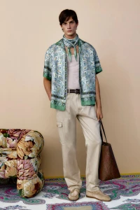Male model wearing a paisley print shirt and neck scarf with light trousers holding a tote bag in Etro S/S 26 Men's Lookbook.
