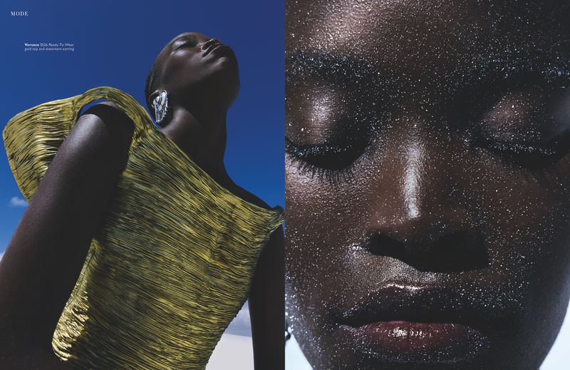 Close-up portrait of a Black woman with sparkling glitter on her face against a bright blue sky background.