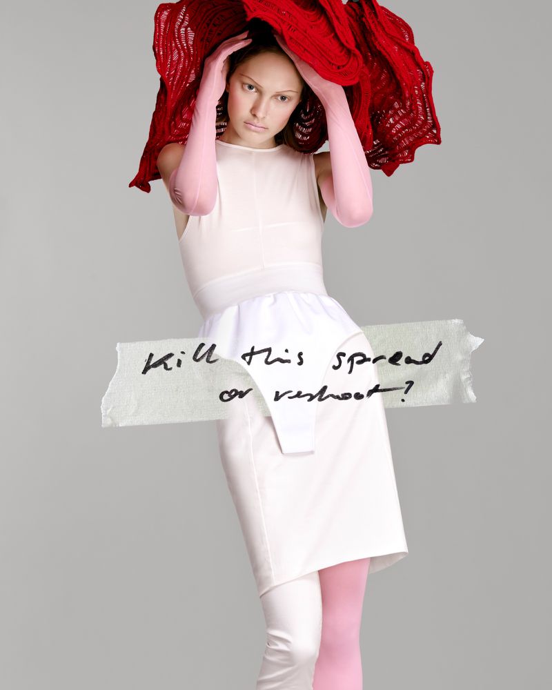 Model wearing a white dress, pink gloves, and a large red textured headpiece with a tape overlay reading 'Kill this spread or reshoot?'.