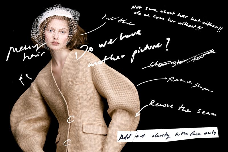 Model Viktoria Wirs wearing a structured beige coat with balloon sleeves and a netted veil hat against a black backdrop with markup text.