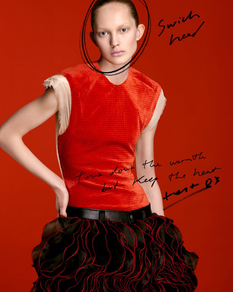 Model Viktoria Wirs in a textured red sleeveless top and ruffled black skirt posing against a bright red studio backdrop with handwritten notes.
