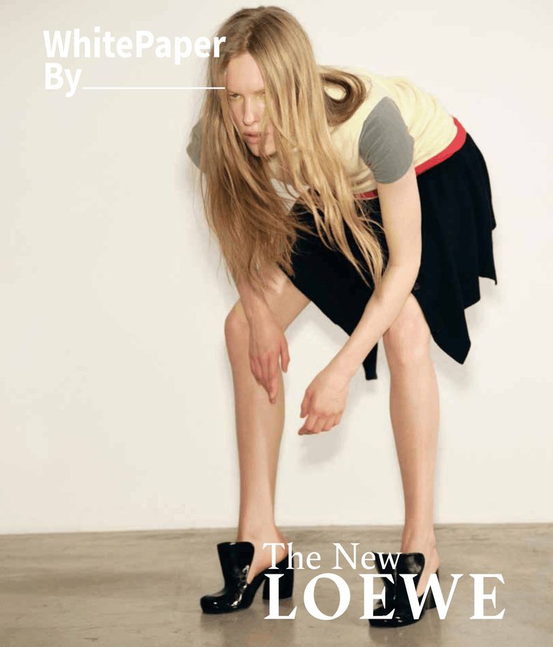 Model Leanne De Haan poses bent forward wearing a color-blocked top, black skirt, and black mules against a white studio wall.
