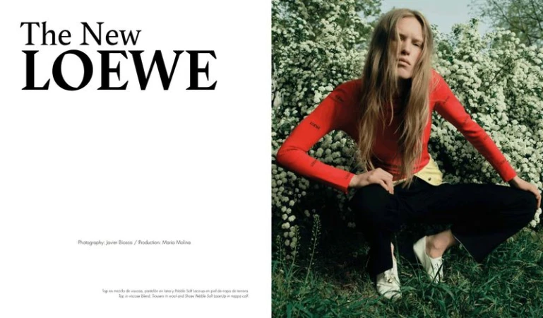 Model Leanne De Haan in a red long-sleeve top and black trousers crouching in front of blooming white bushes in a fashion spread.
