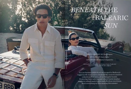 Man wearing a cream shirt and sunglasses standing beside a vintage red convertible car with a woman seated inside