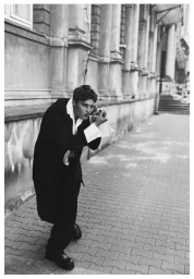 Black and white portrait of a man leaning against a classical stone building exterior wearing a dark suit