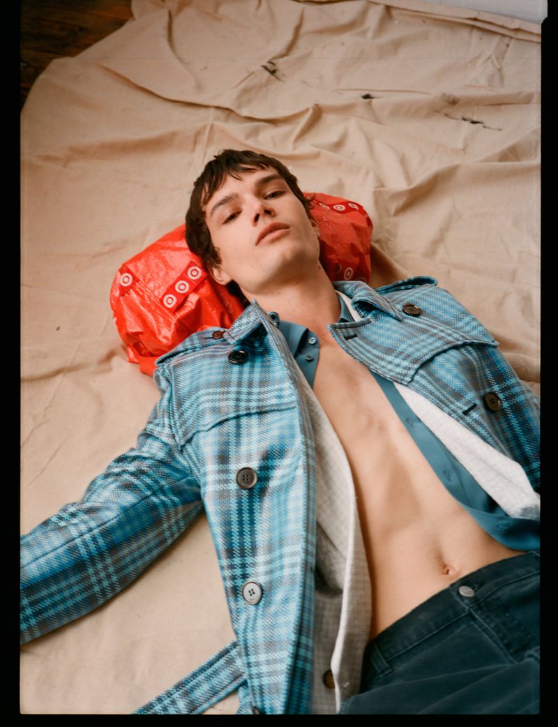 Model Ian Jeffrey lying on a beige canvas backdrop wearing an open blue plaid coat for L'Officiel Hommes Malaysia.