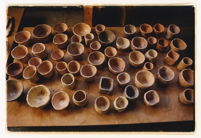 Collection of handmade ceramic cups and small clay bowls arranged across a wooden board.