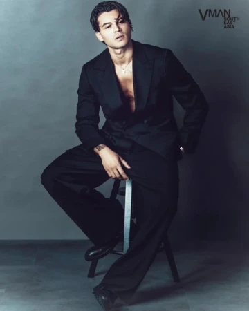 Antonio Medugno seated on a stool wearing a black tailored suit with an open jacket against a grey studio backdrop.