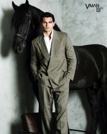 Man wearing a grey suit standing next to a black horse in front of a textured grey wall