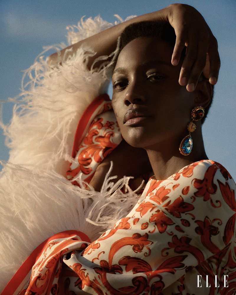 Model wearing a patterned orange and white dress with feather trim against a clear blue sky